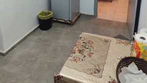 A compact room with a grey refrigerator, a trash bin, and a floral-patterned rug.