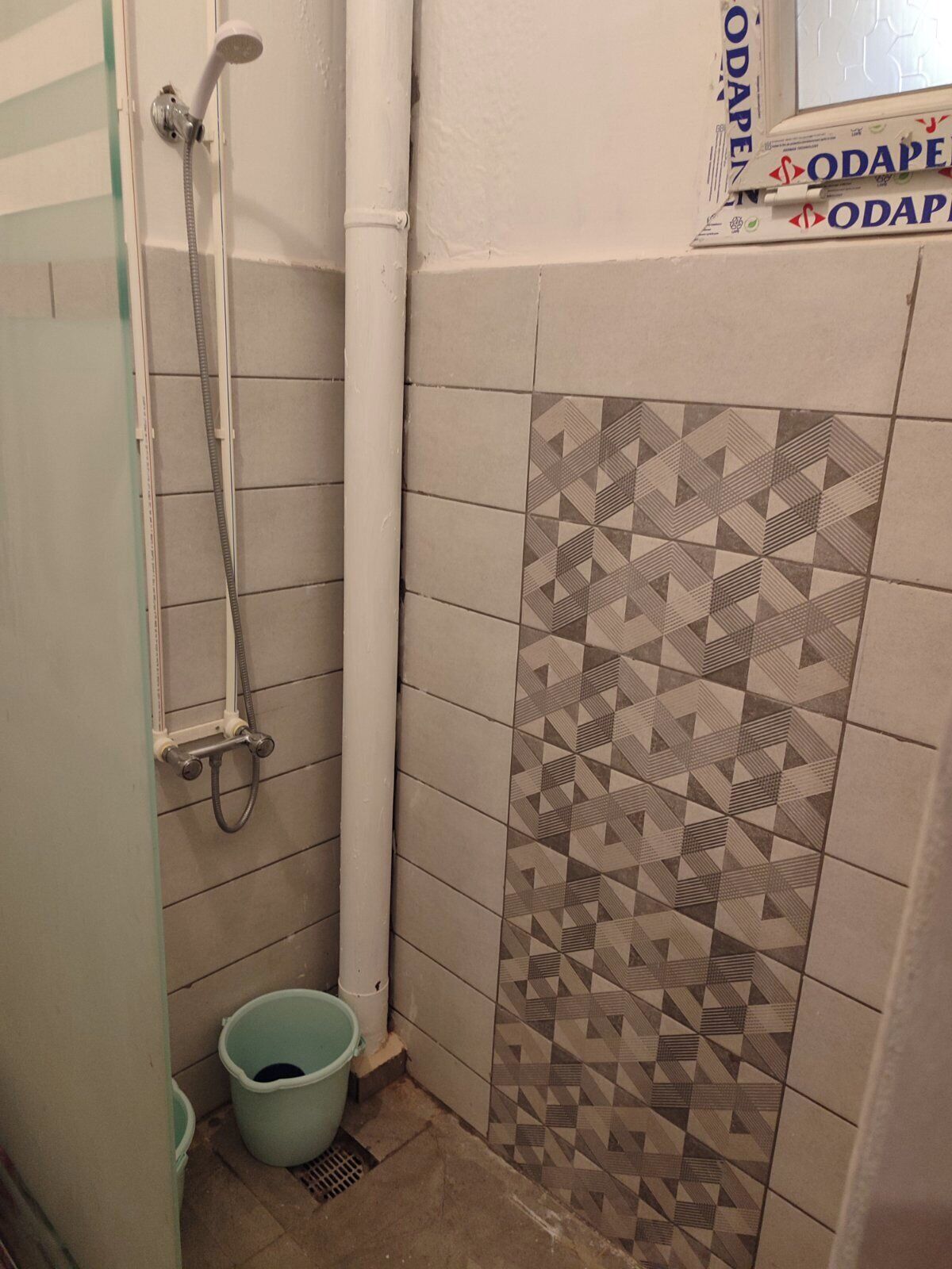 A bathroom with a shower, a patterned tile wall, and a bucket on the floor.