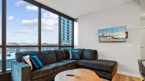 A modern living room with a large window, a sectional sofa, a round coffee table, and a painting on the wall.