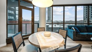A modern living room with a round table, a sofa, and large windows offering a city view.