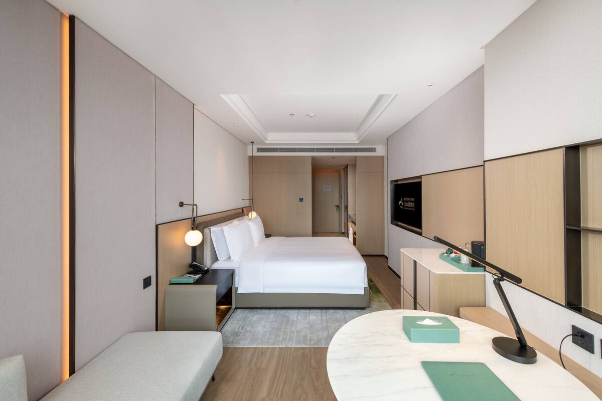 Ein modernes Hotelzimmer mit Bett, Nachttischen, einem Schreibtisch und einem Flachbildfernseher.