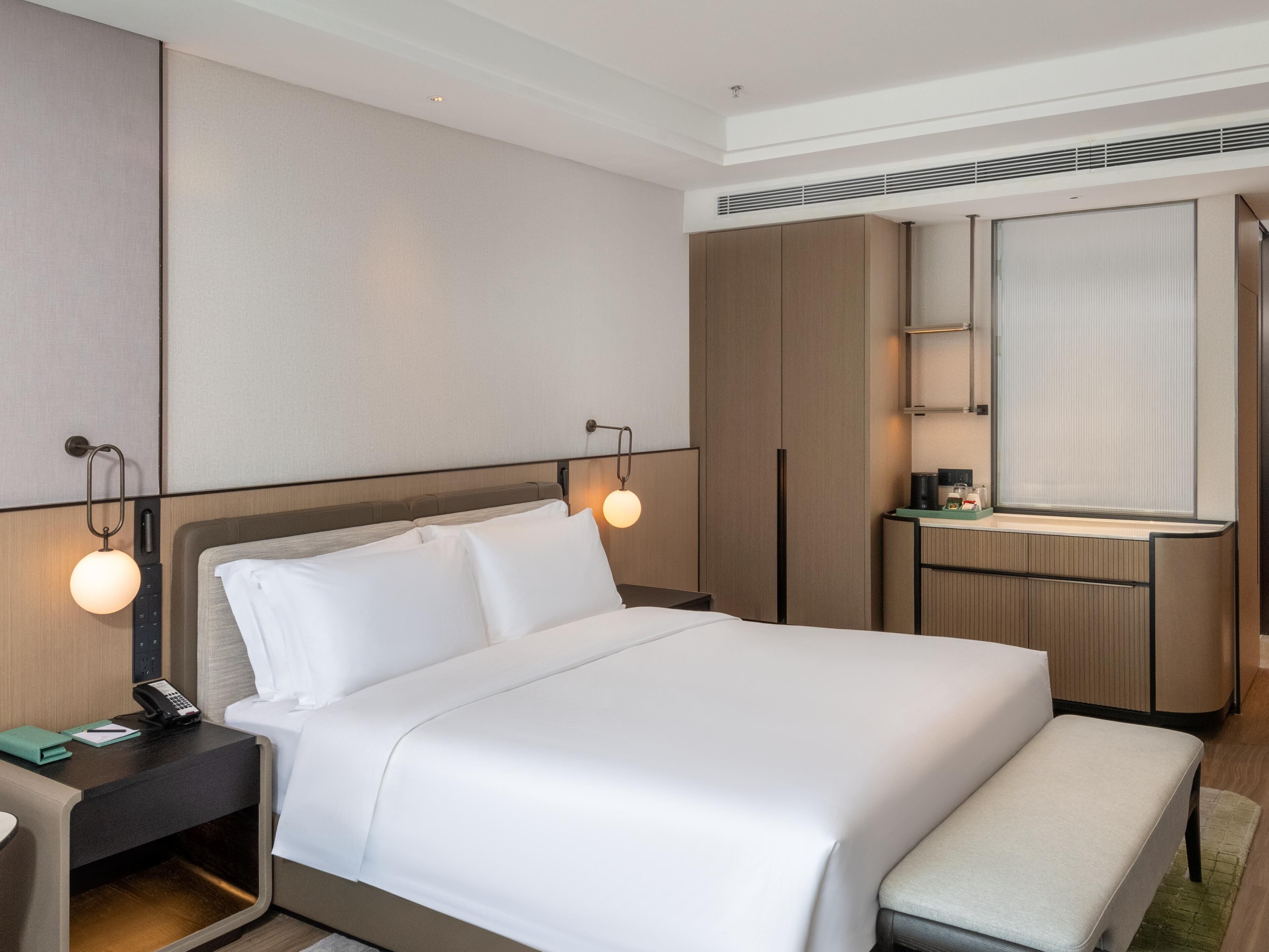 A modern hotel room with a large bed, bedside tables, a desk, and a mirror.