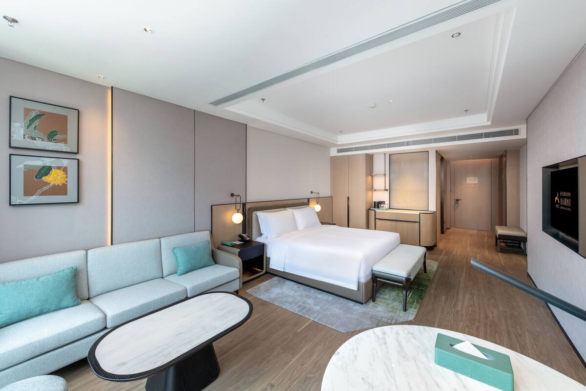 Ein modernes Hotelzimmer mit einem großen Bett, einer Sitzecke, einem kleinen Tisch und einem Fernseher.