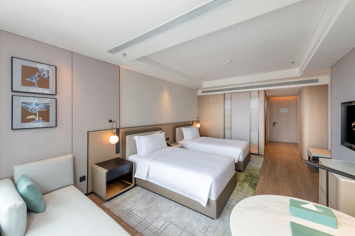 Ein Hotelzimmer mit zwei Betten, einem Sofa, einem Schreibtisch und Bildern an der Wand.