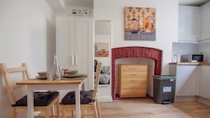 A compact kitchen with a wooden table, chairs, a microwave, and a trash bin.