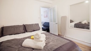A bedroom with a bed, pillows, a rolled towel, a standing heater, and a mirror on the wall.