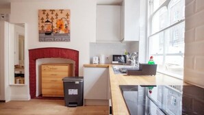 A modern kitchen with a microwave, toaster, and sink. There is a red fireplace, a trash bin, and a window with a view of buildings.