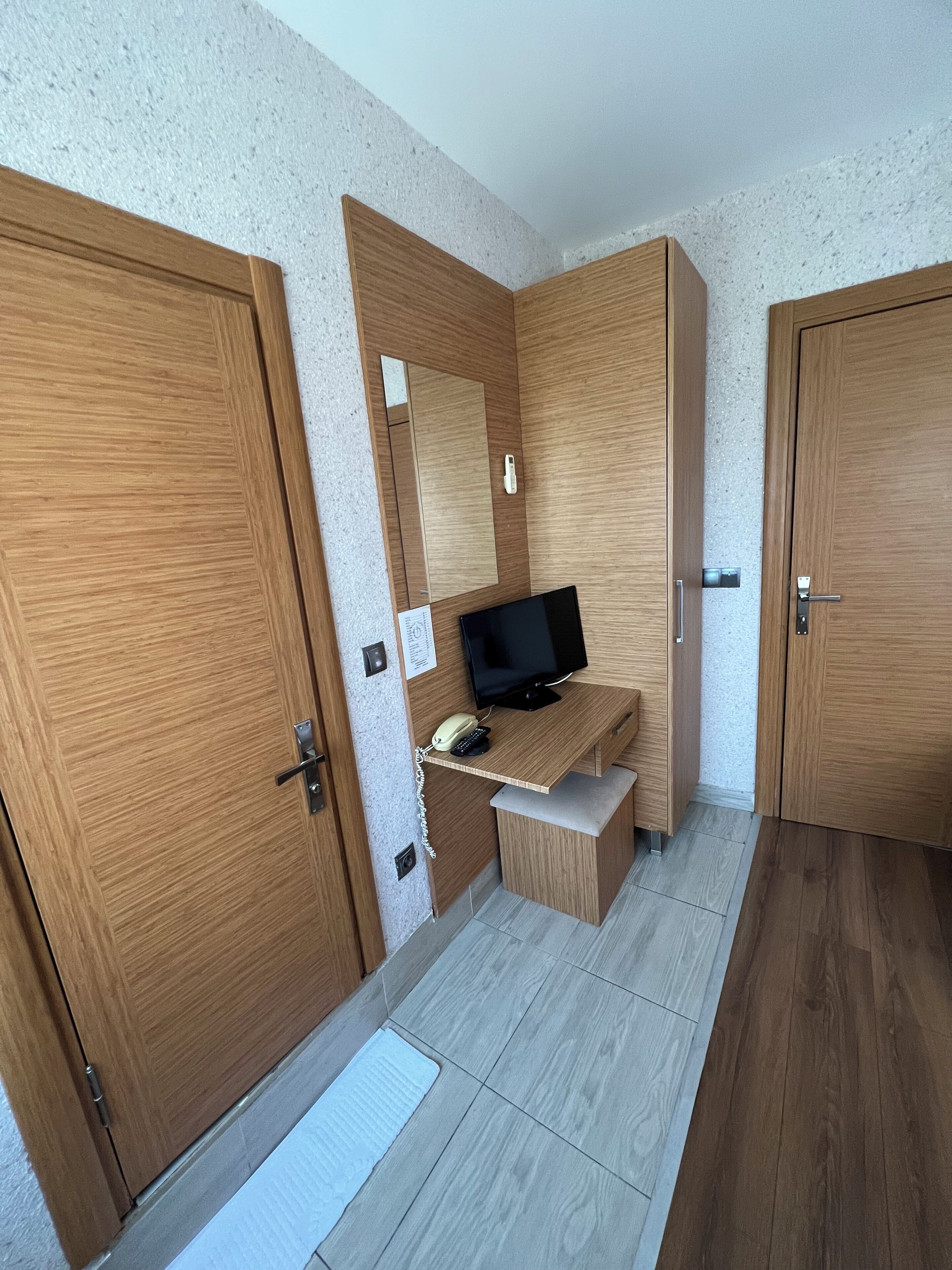 Een hotelkamer met houten deuren, een bureau met een televisie, een telefoon en een spiegel.