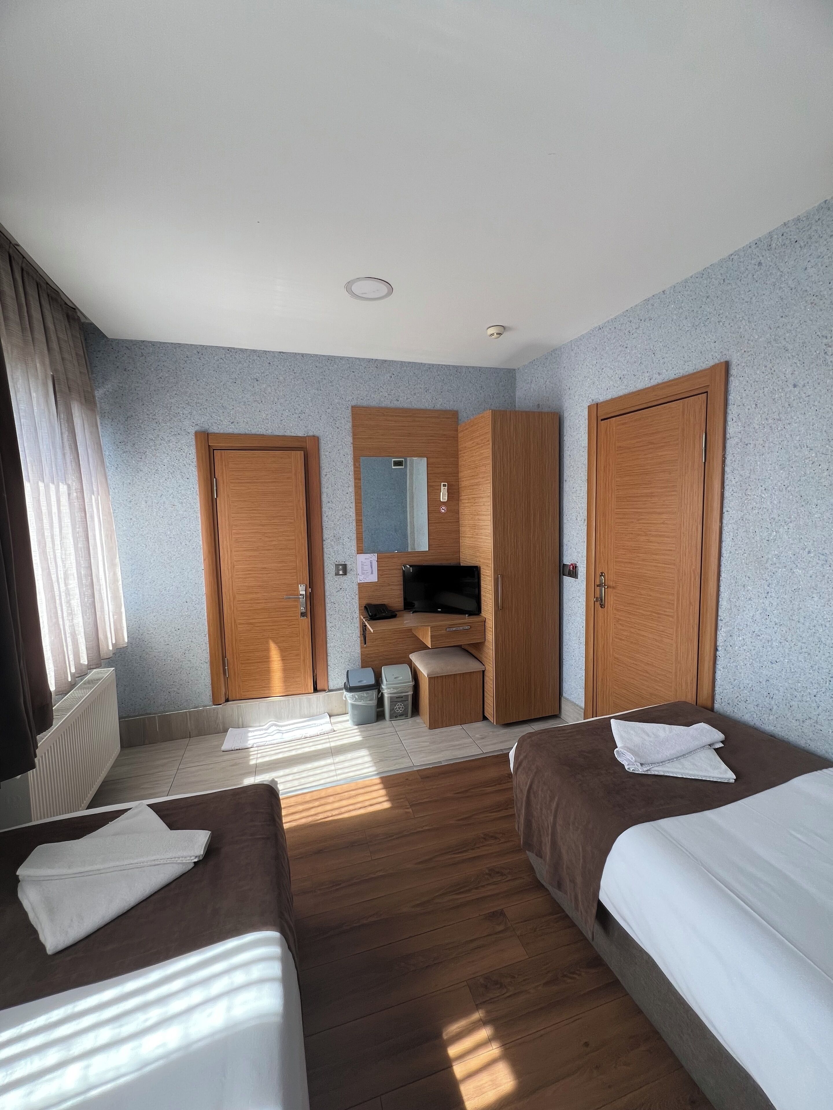 A hotel room with two beds, a desk with a TV, and a wardrobe.