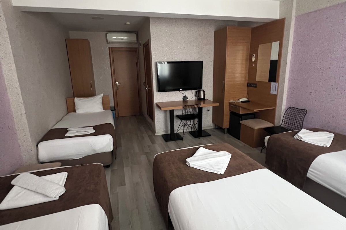 A hotel room with four single beds, a desk with a flat-screen TV, a coffee machine, and a small seating area.