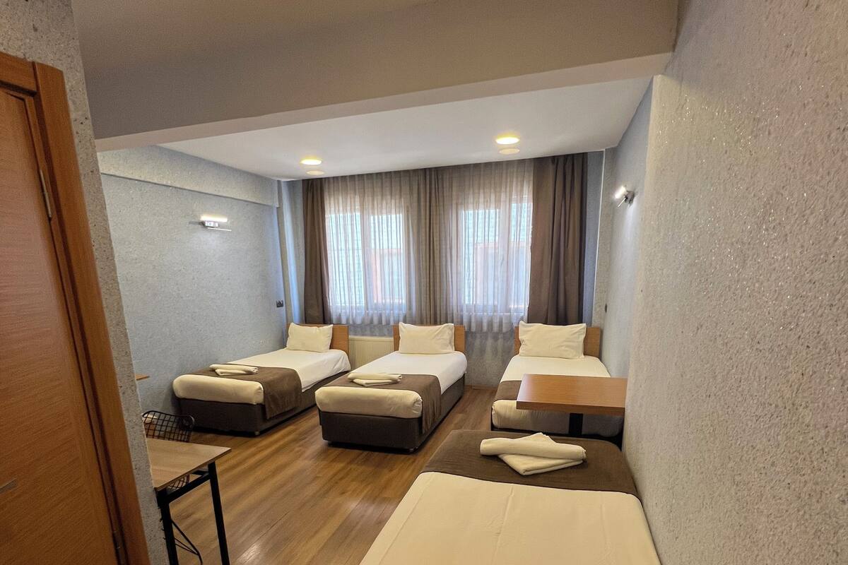 A hotel room with three single beds, a small table, and a sofa.