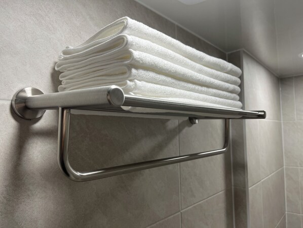 A metal towel rack with folded white towels in a bathroom with tiled walls. - StayDucksan Hotel (Suwon)