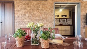 A dining table set with clear glasses, a white plate with 'Spaghetti' written on it, and three woven baskets containing plants and tomatoes. - Beach House Roccalumera (Roccalumera)