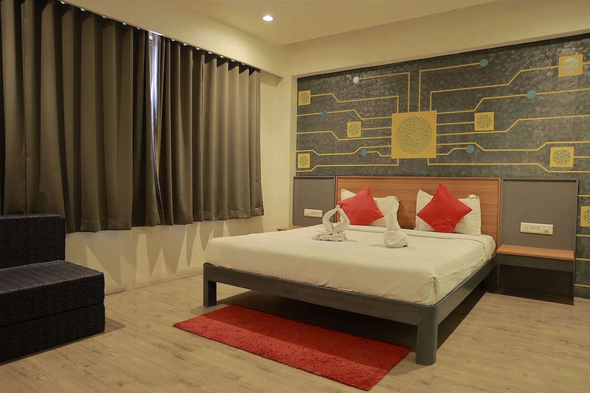 A modern hotel room with a bed, a red rug, a wooden nightstand, and a wall with a circuit board design.