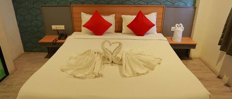 Una cama bien hecha con una disposición de toallas en forma de corazón, un cabecero de madera y una pared con un diseño estampado.