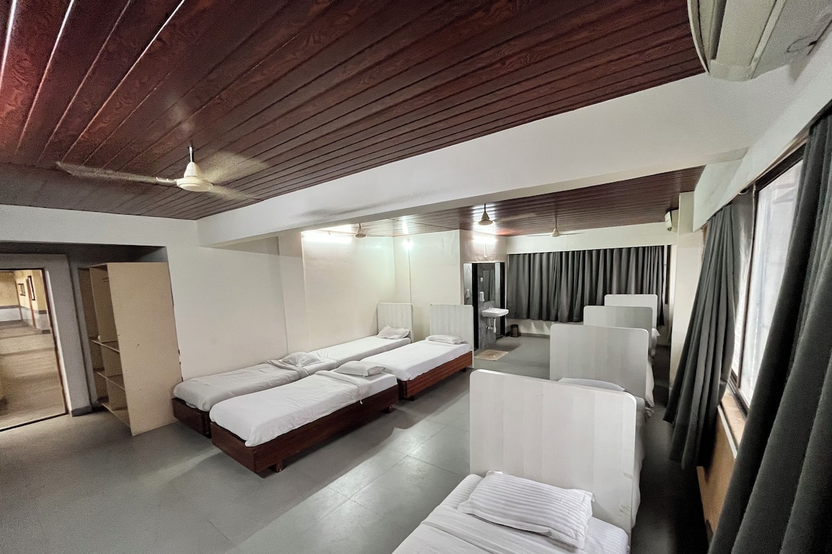 A hotel room with two single beds, a small bathroom, and a seating area with curtains.