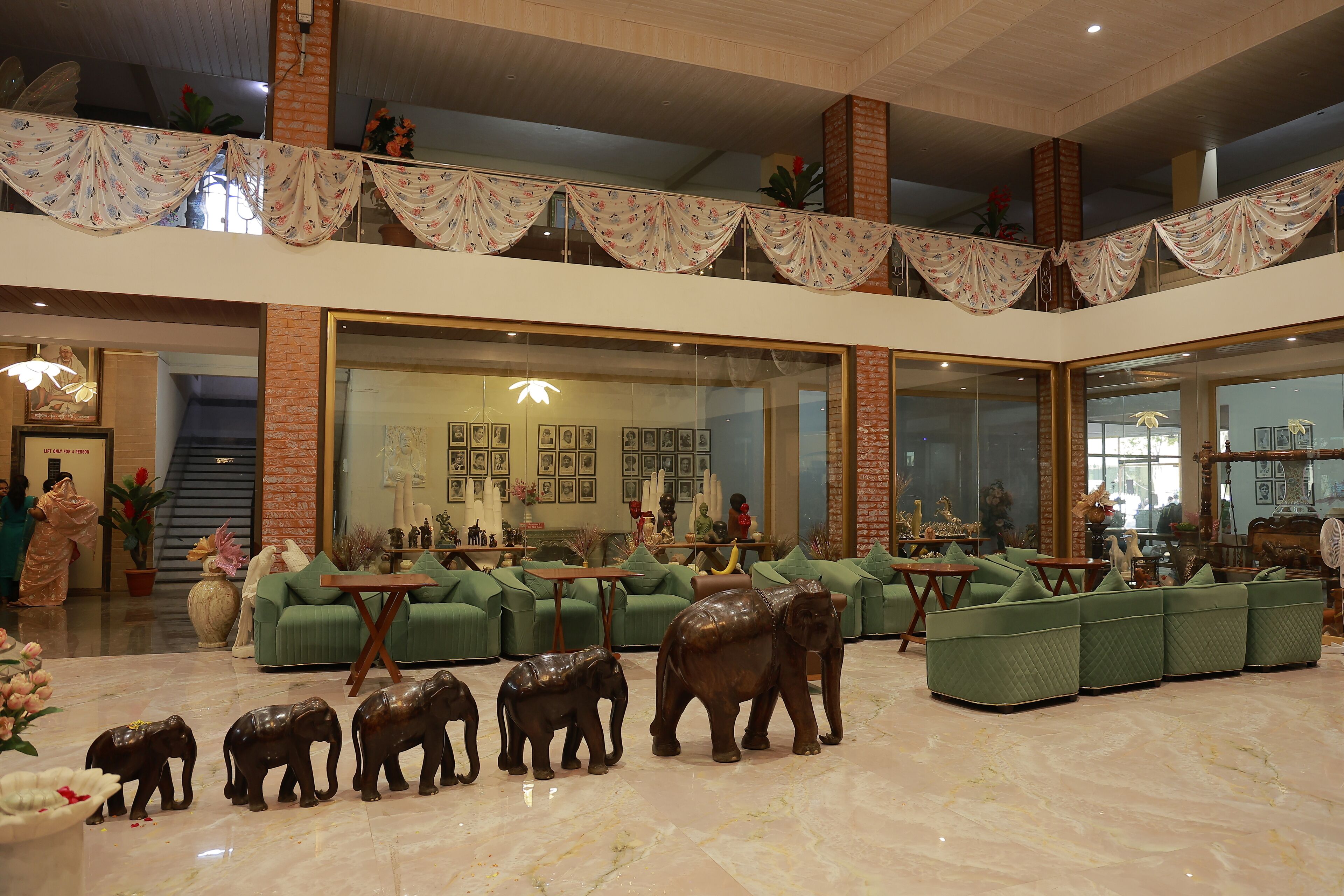 Un hall d’entrée spacieux, avec des canapés verts, un grand miroir et des statues d’éléphants décoratives.