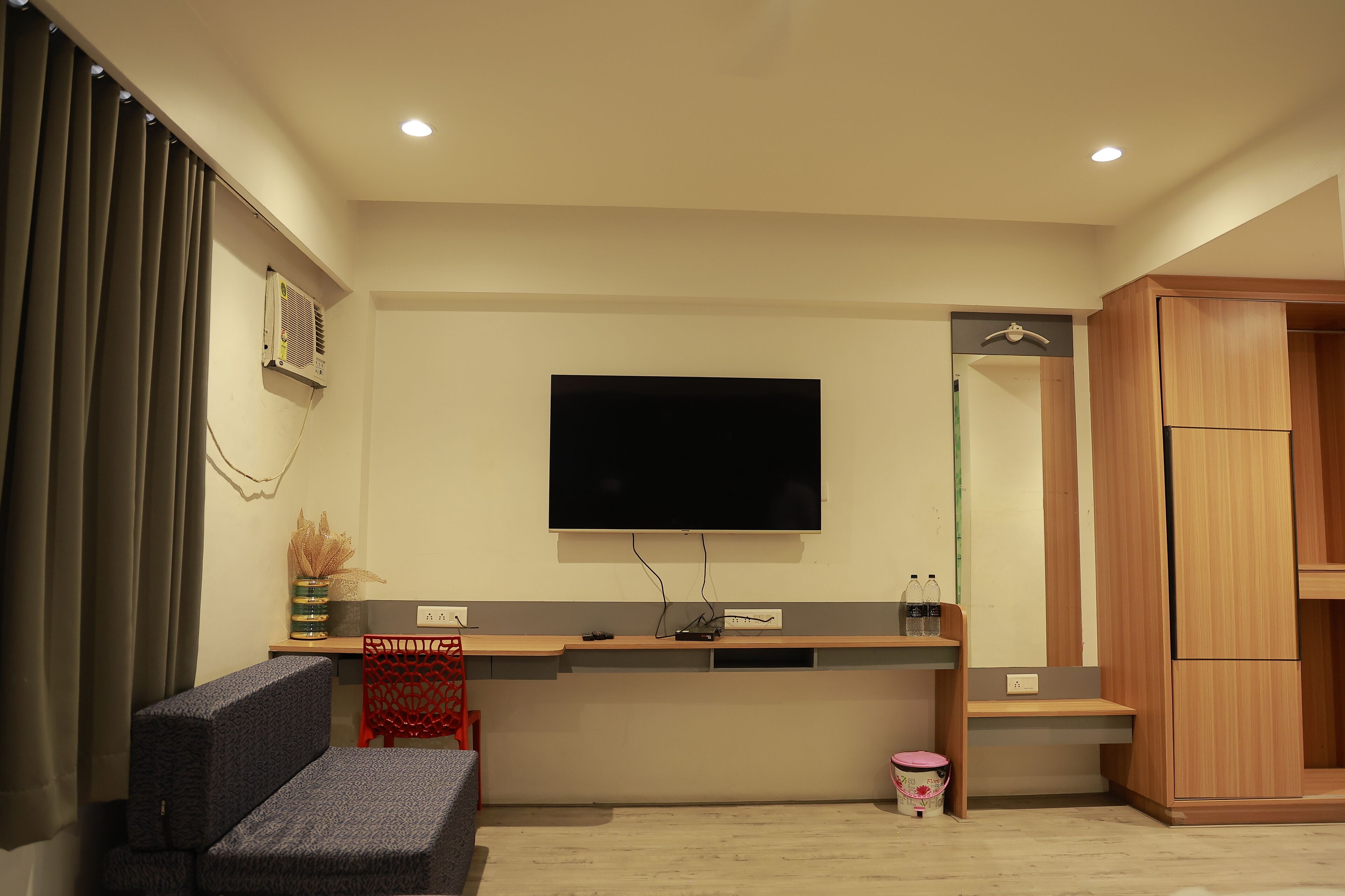 A modern living room with a flat-screen TV mounted on the wall, a grey sofa, a red chair, and a wooden cabinet.