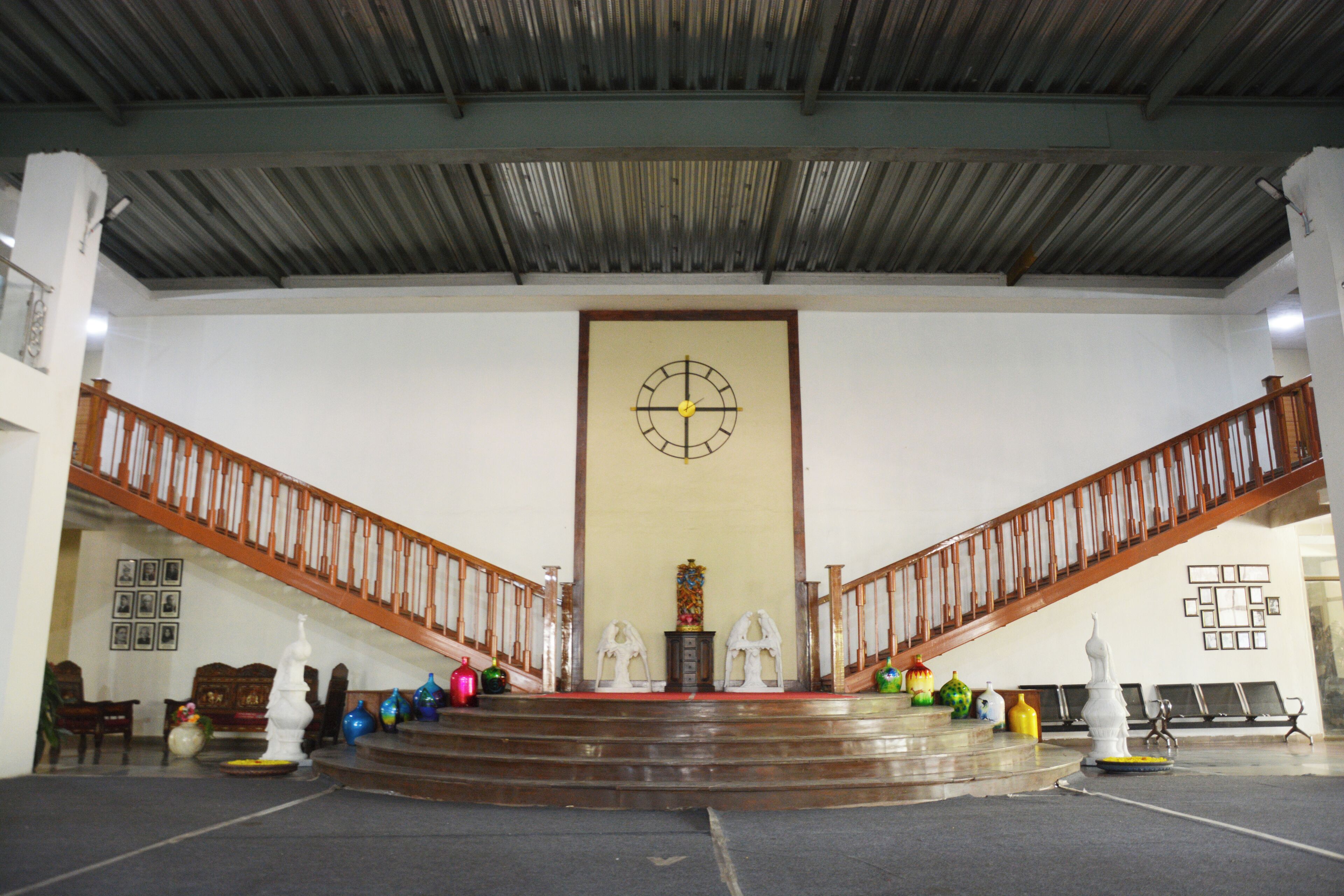 A spacious interior with a central staircase, wooden railings, and a large wall clock.