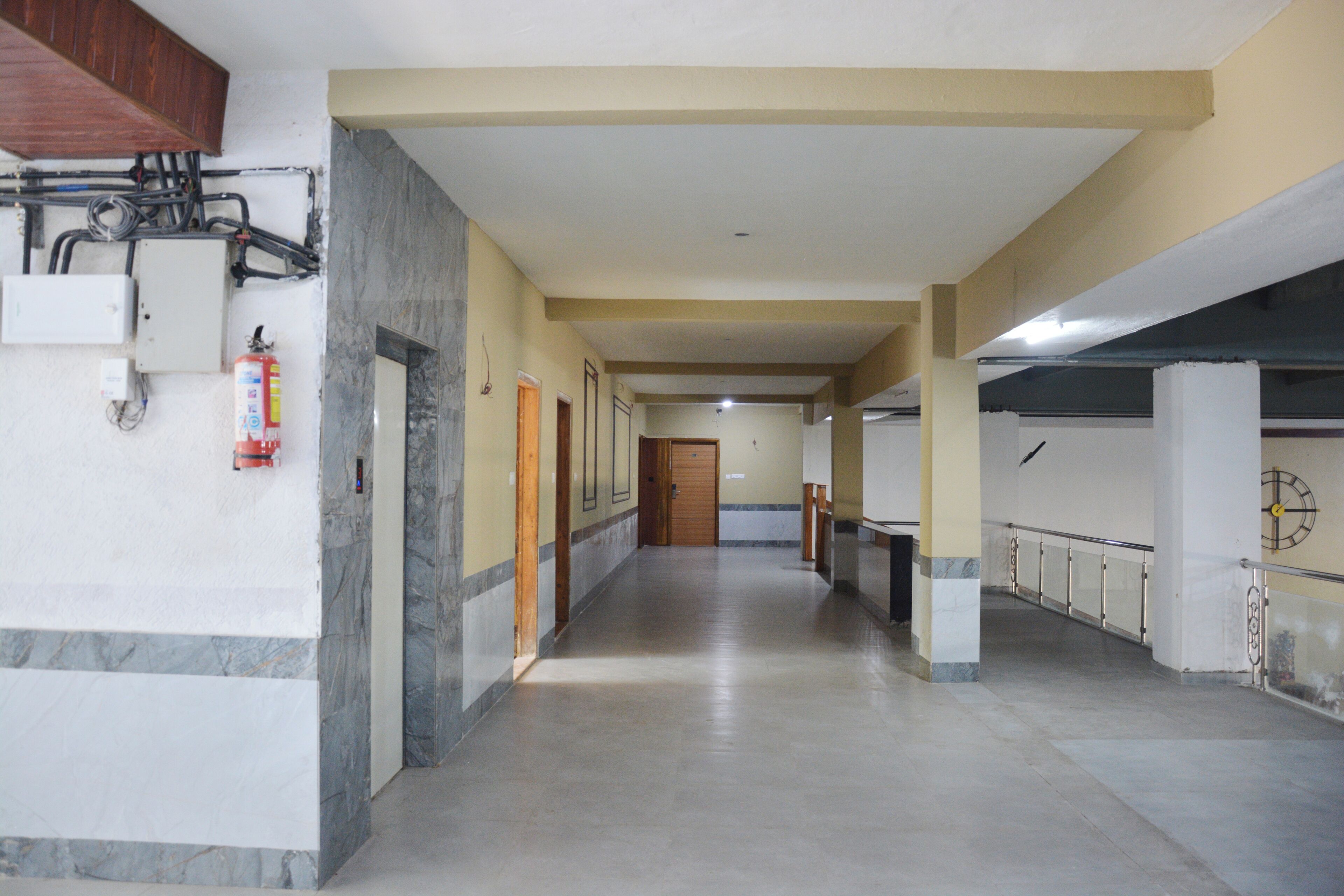 A long, narrow hallway with a marble floor, wooden doors, and a fire extinguisher on the left.