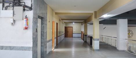 A long, narrow hallway with a marble floor, wooden doors, and a fire extinguisher on the left.