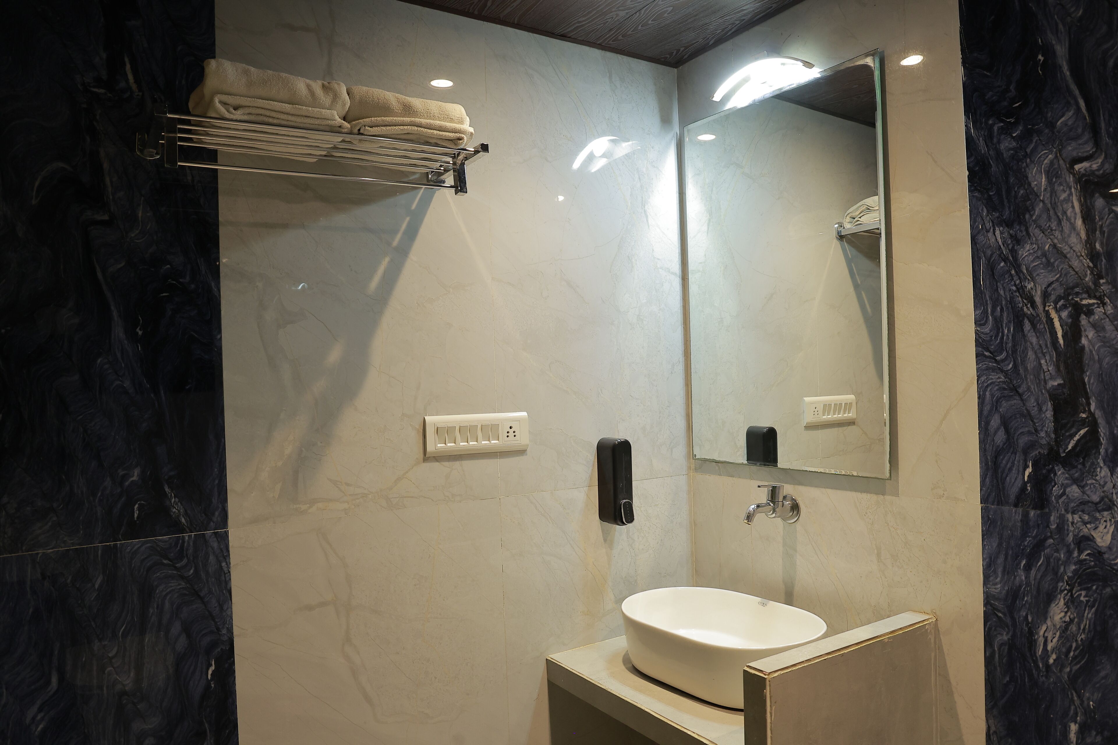 Un baño moderno con pared de mármol, lavamanos, toallero y espejo.