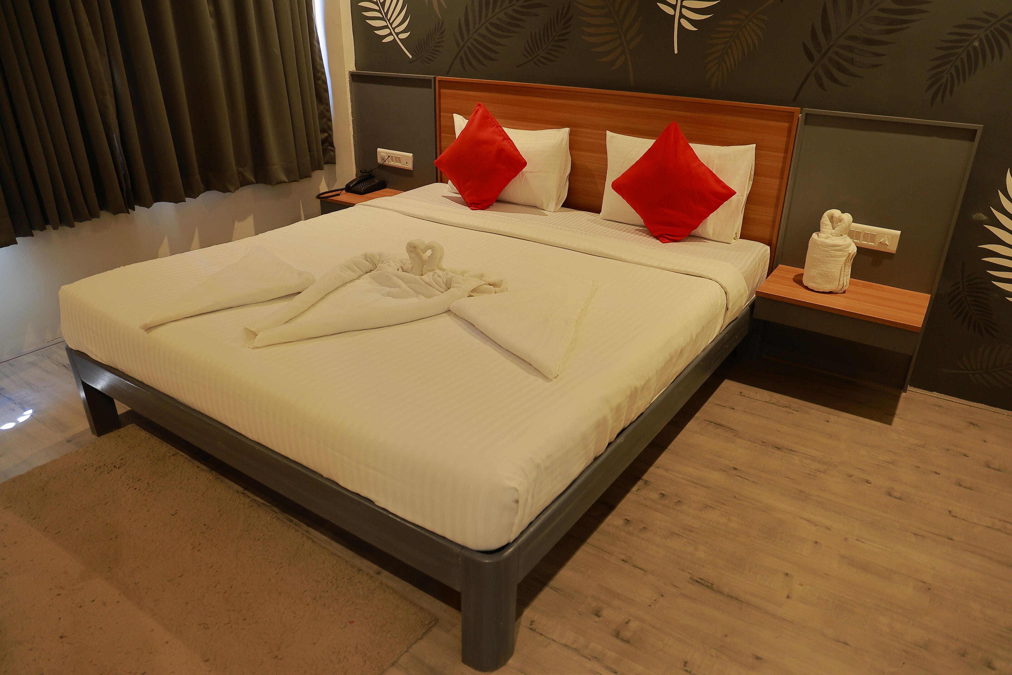 A neatly made bed with white linens, red and white pillows, and a towel arranged on the bed.