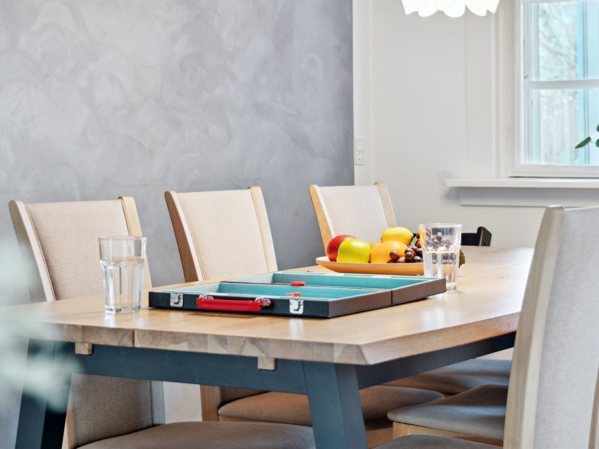 A dining table with a board game, glasses, and a fruit bowl.