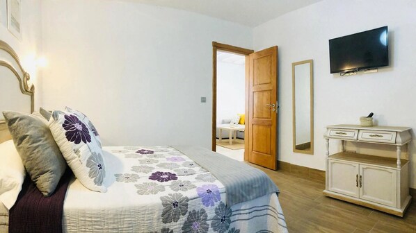 A bedroom with a bed, a dresser, a television, and a door leading to another room.