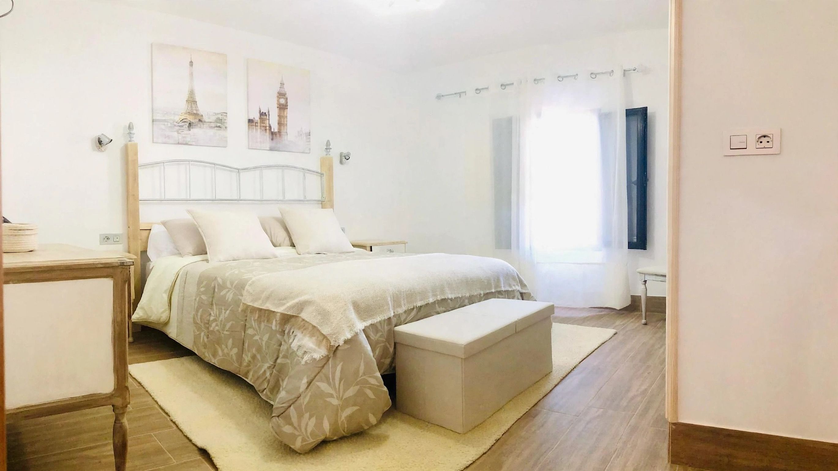 A bedroom with a bed, bedside tables, a bench, and artwork on the wall.