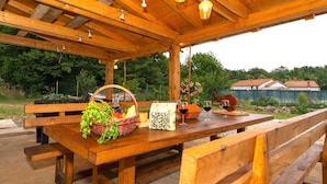 An outdoor wooden pavilion with benches and tables, surrounded by greenery and a fence. - Luxurious Villa in Ružići Croatia with Private Pool and Garden (Ružici)