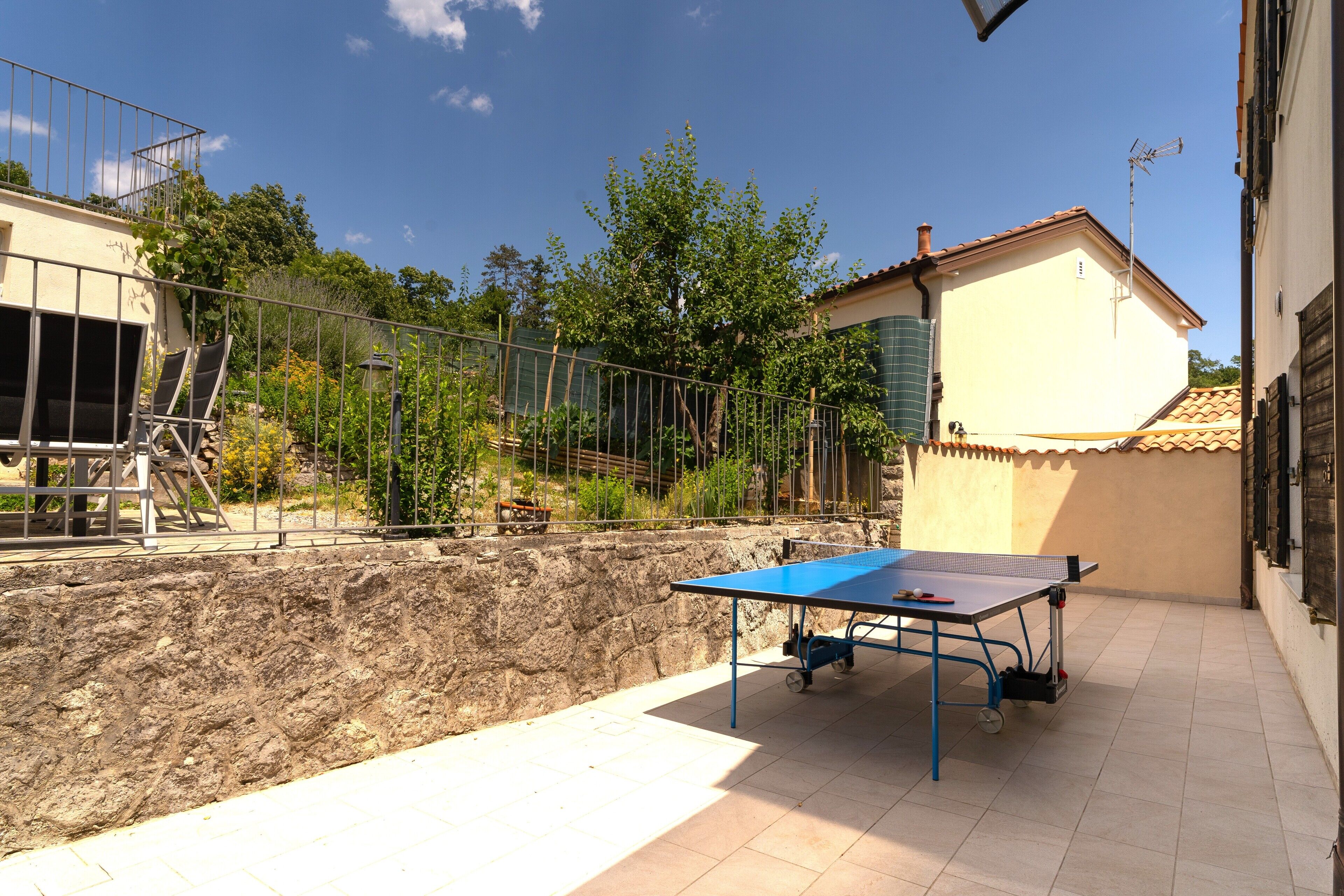 An outdoor table tennis table set up on a patio with a stone wall and a building in the background.