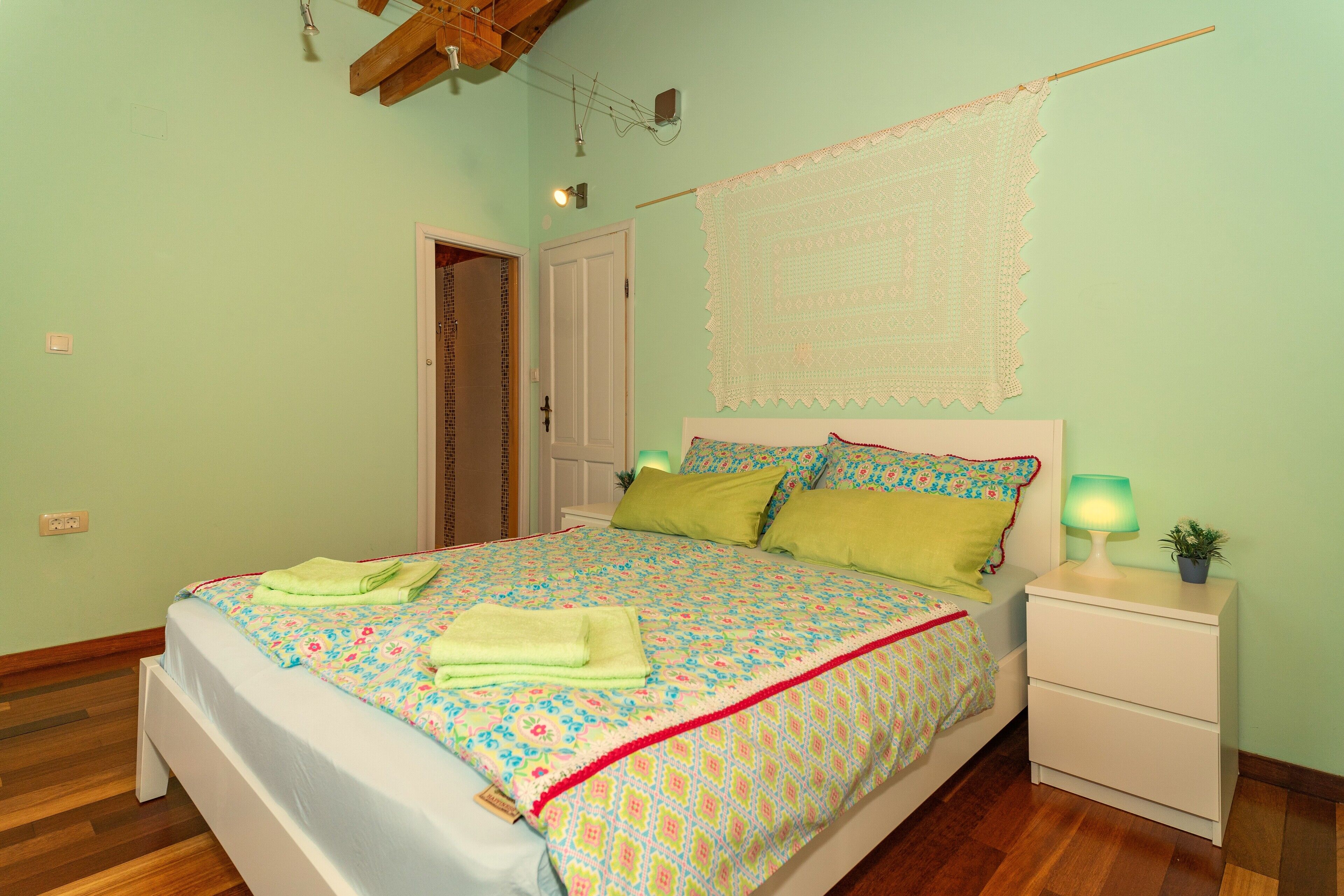 A neatly made bed with a floral bedspread, a bedside lamp, and a small potted plant on the nightstand.