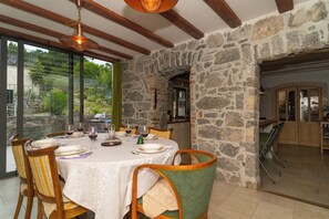 A dining area with a stone wall, wooden beams, and a table set for four. - Villa Salvia with pool (Ružici)