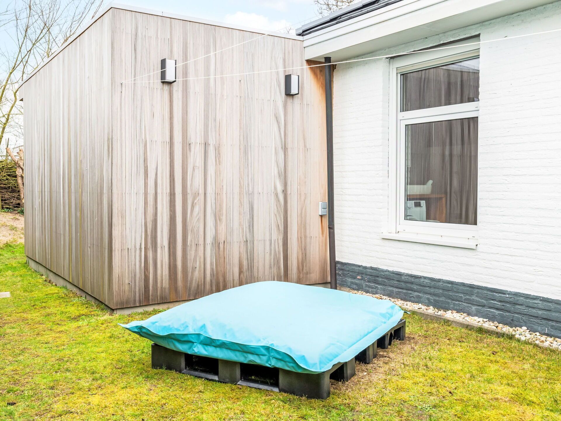 A wooden shed with a door, a window, and a blue tarp on the ground.