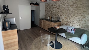 A modern living room with a sofa, coffee table, and a kitchen area with wooden cabinets and a stone wall. - Love Room with private spa  (Le Perrier)