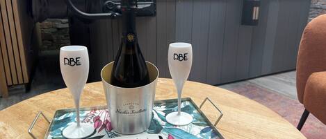 Une table avec une bouteille de champagne et deux verres portant l’inscription « DBE », le tout disposé sur un plateau orné de motifs floraux.