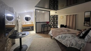 A modern bedroom with a large bed, a desk, and a bathroom with a mirror and vanity. - Love Room with private spa  (Le Perrier)