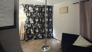 A room with a black armchair, a floor lamp, a floral curtain, a wooden chair, and a wall with a 'Love' sign. - Love Room with private spa  (Le Perrier)