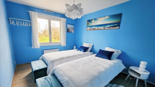 Ein Schlafzimmer mit zwei Betten, einem Fenster, einem Gemälde und einem kleinen Tisch.