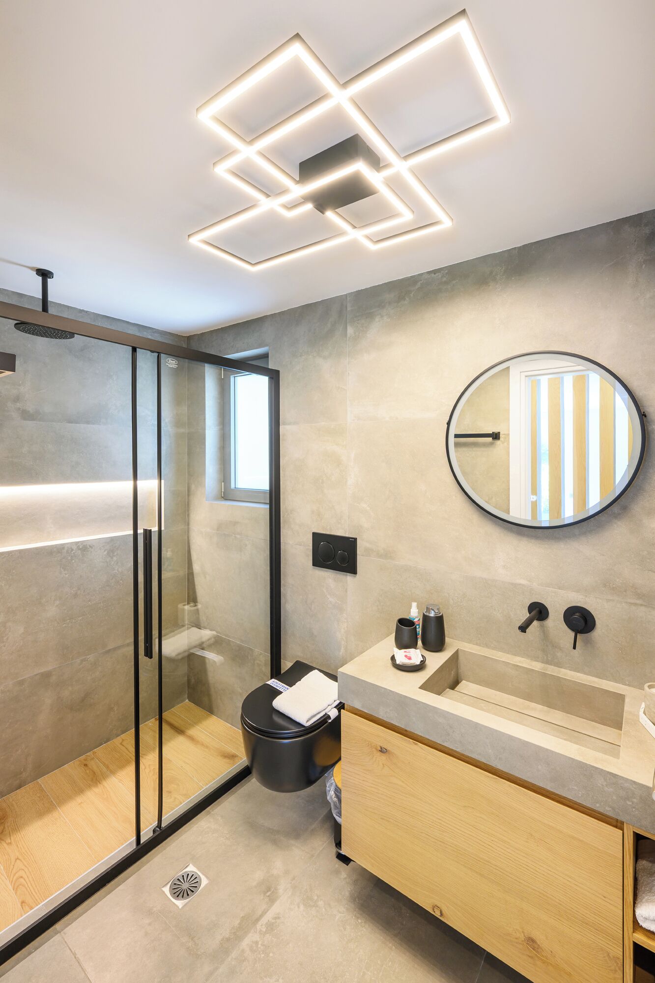 A modern bathroom with a glass shower enclosure, a round mirror, and a wooden vanity.