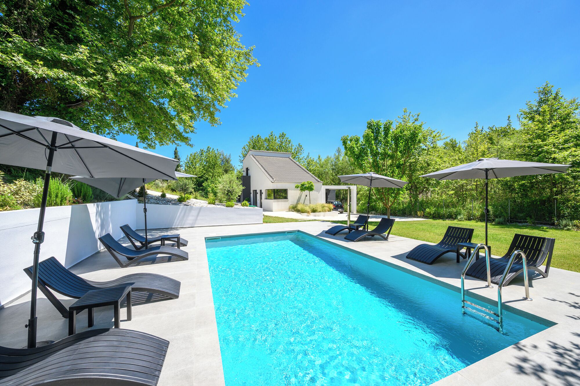 A rectangular swimming pool with clear blue water, surrounded by lounge chairs and umbrellas.