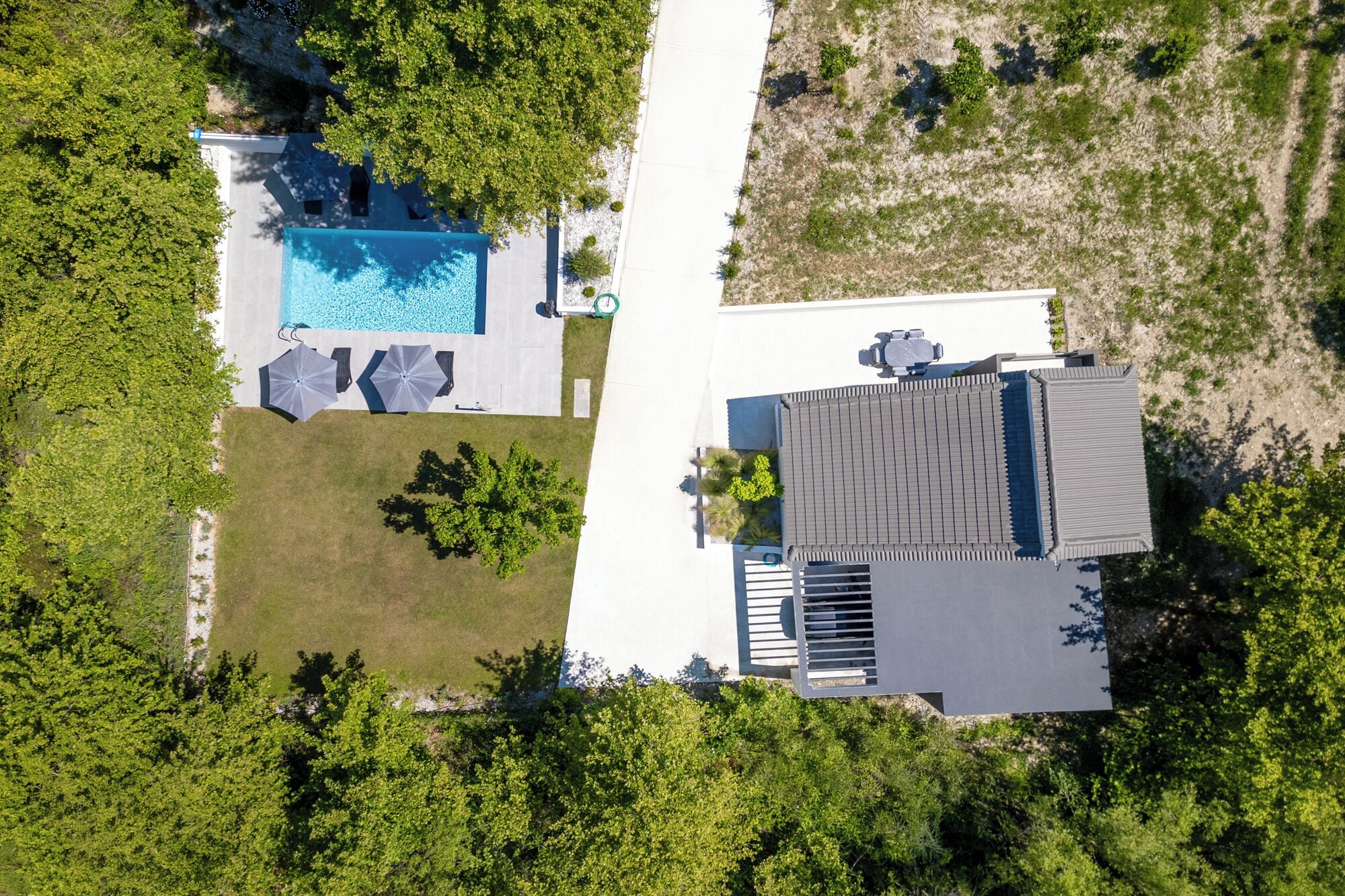 En vy från ovan av ett hus med en swimmingpool, en uteplats med parasoller och en välskött gräsmatta.