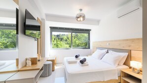 Een moderne slaapkamer met een bed, nachtkastjes, een televisie en een raam met uitzicht op groen.