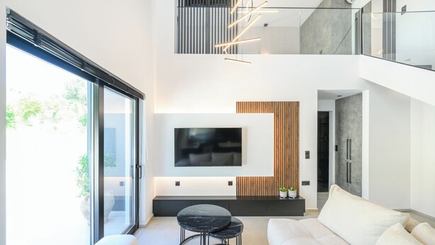 Een moderne woonkamer met een grote flatscreen televisie aan de muur, een zwart marmeren salontafel en een witte bank.