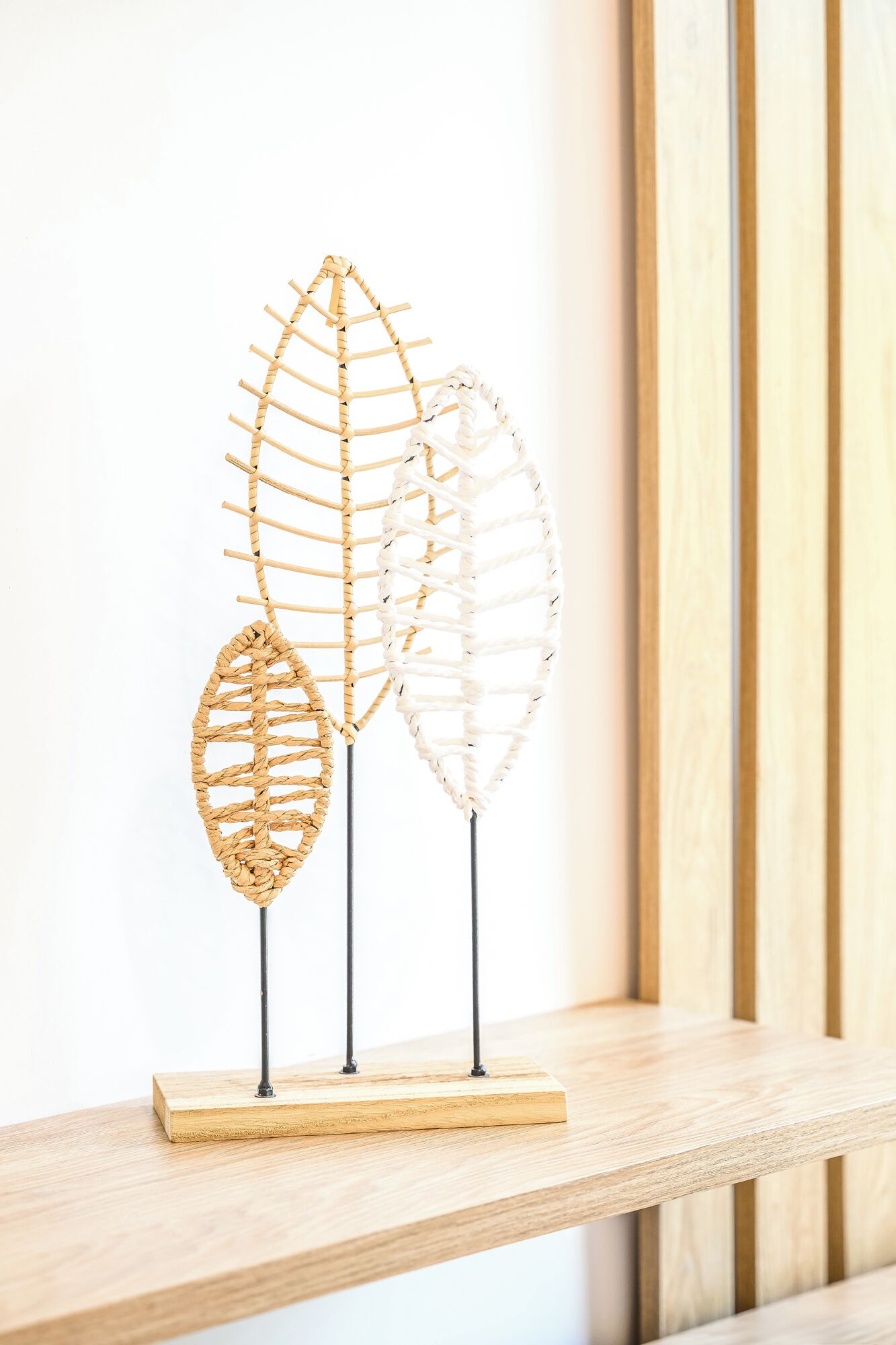 Three woven plant wire sculptures on a wooden shelf.