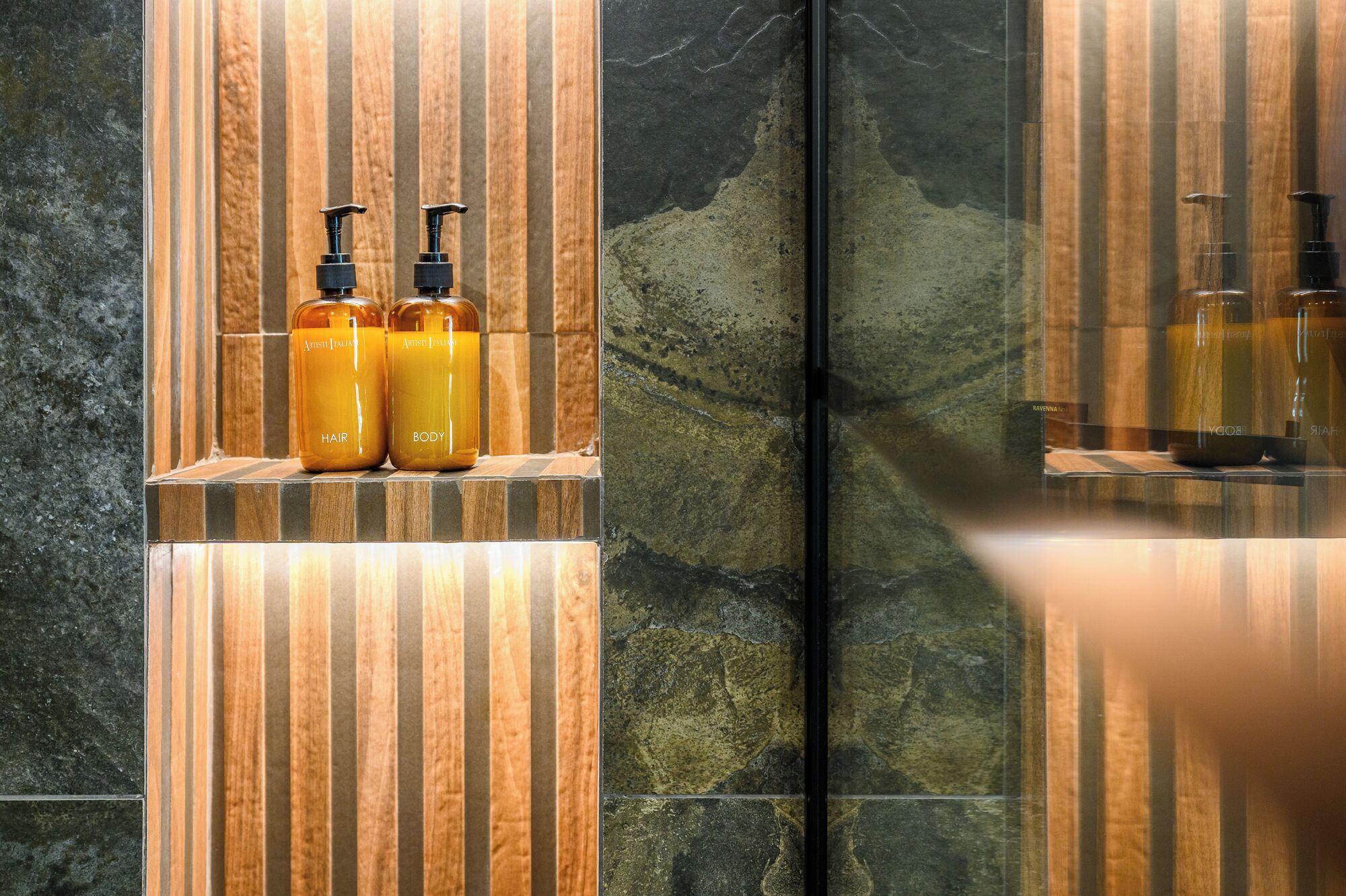 A bathroom with a mirror, two bottles labeled "Hair" and "Body" on a shelf, and a wooden panel design.