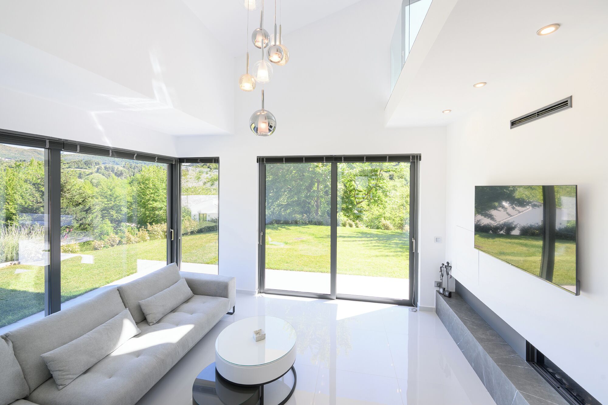 Un salon moderne avec un canapé, une table basse et de grandes fenêtres donnant sur un paysage verdoyant.
