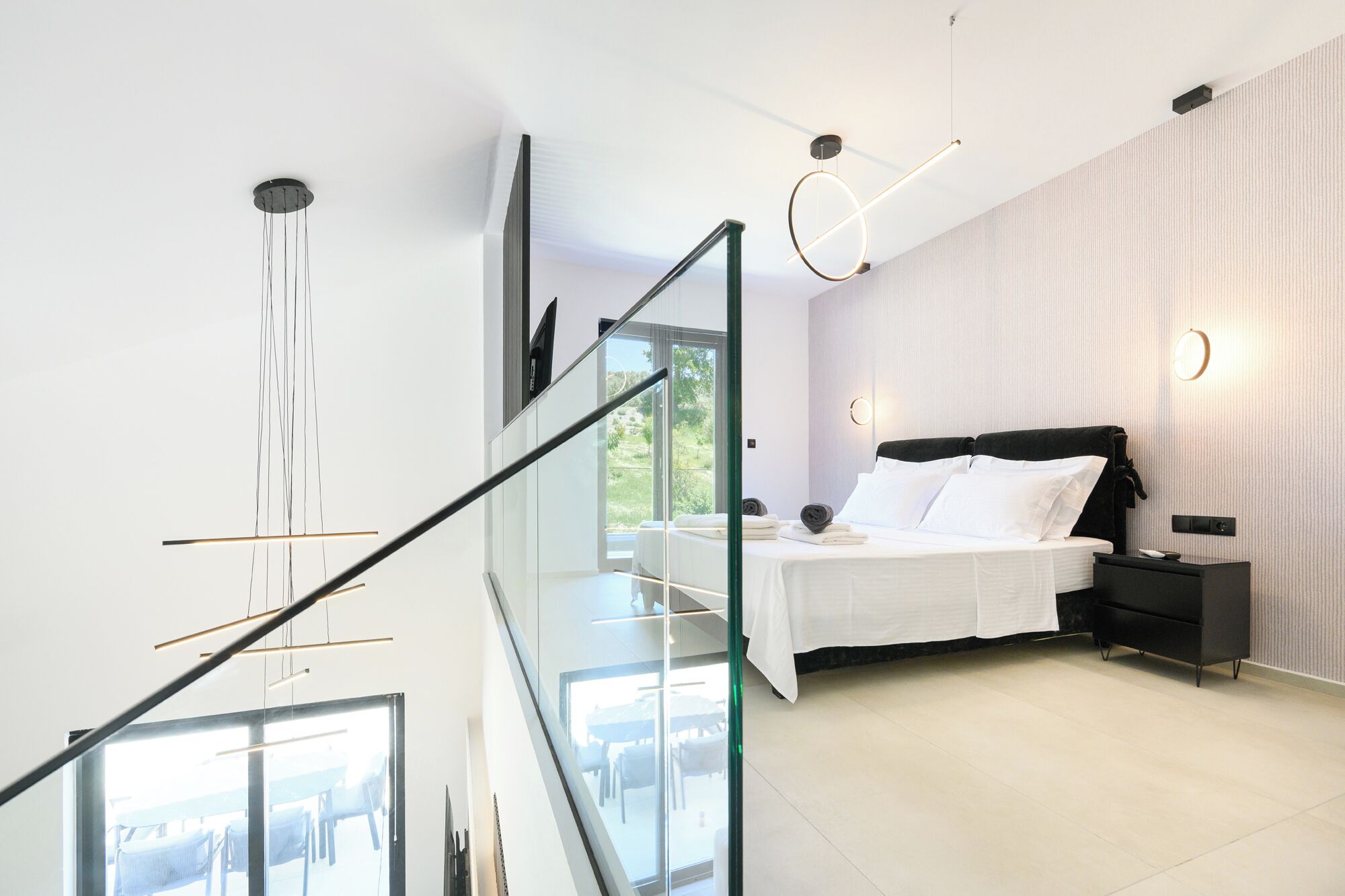 Un dormitorio moderno con cama, mesita de noche y vistas al exterior a través de un ventanal.