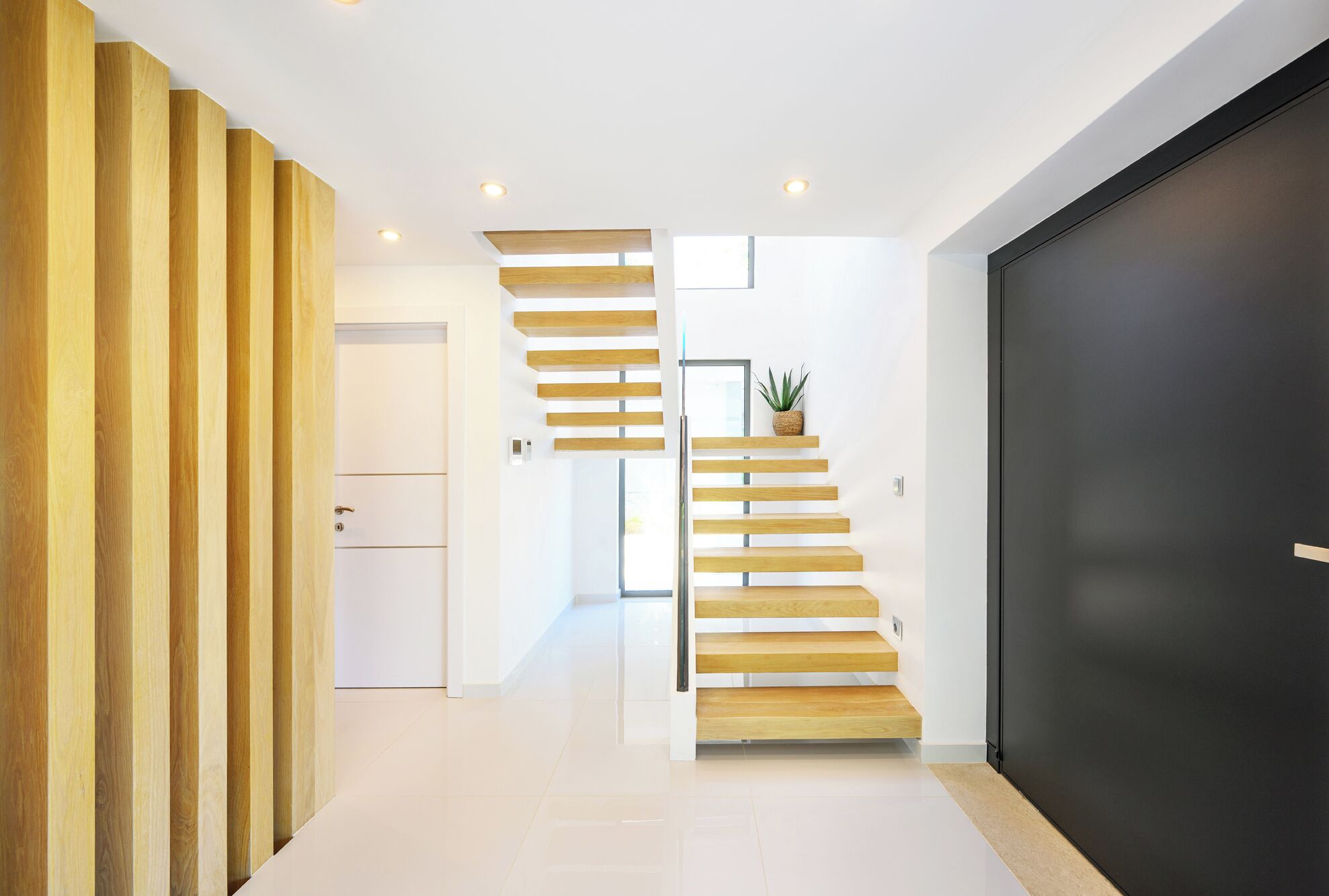 Un intérieur moderne avec un escalier, une porte sombre et un mur blanc.